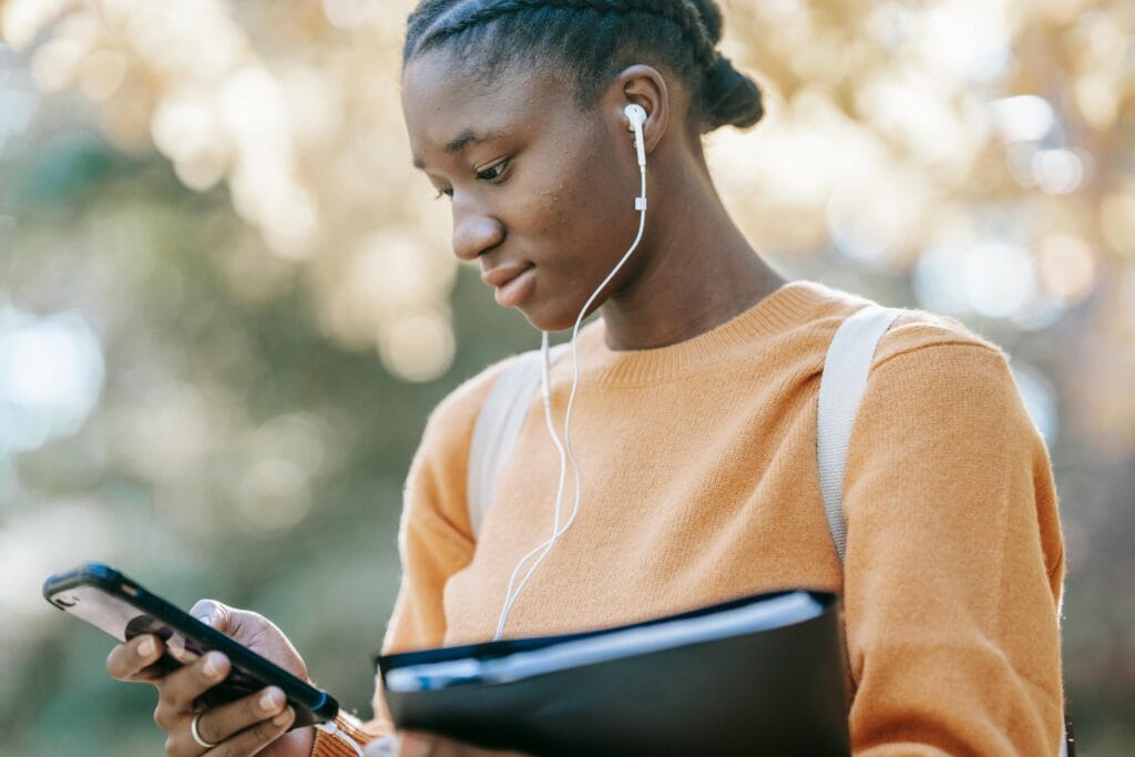 Young female looking at her phone while holding a file and putting on her earphones