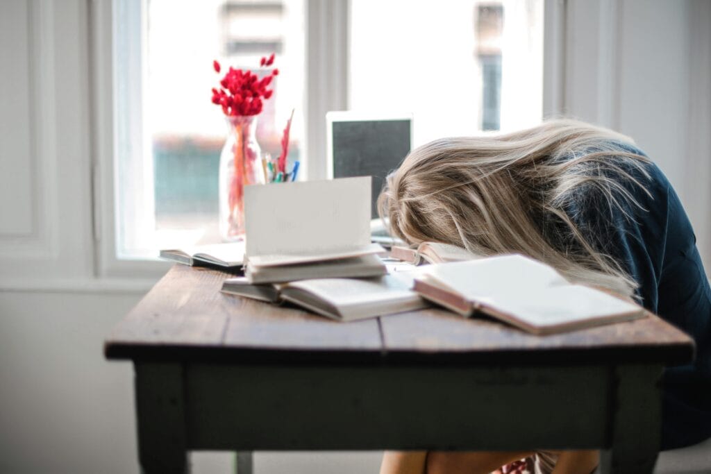 Student Balancing Work and Studies - Photo by Andrea Piacquadio from Pexels A young woman sitting at a table with a laptop and coffee, appearing tired and overwhelmed while studying or working