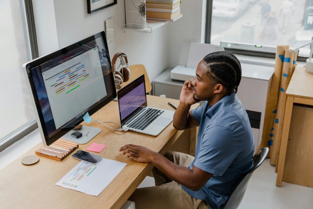 A male freelancer sitting in front of a computer and a laptop editing a document