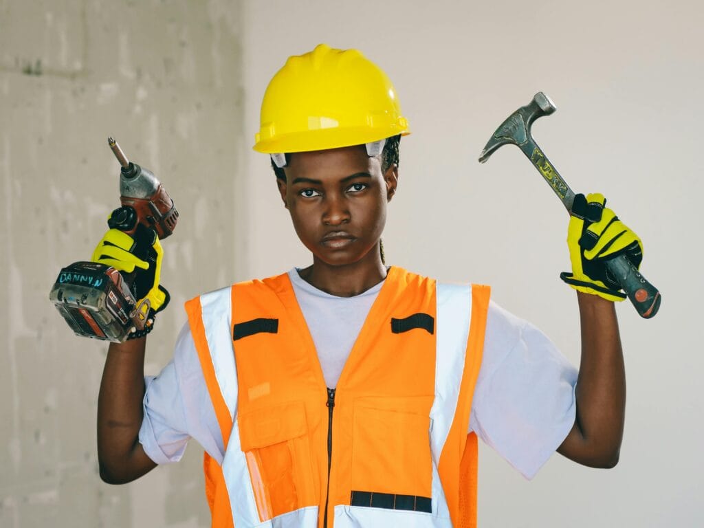 A woman plumber holding a hammer and a hand drill